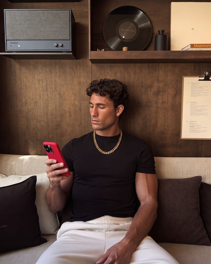 Man in a black T-shirt wearing the gold Billie Cuban Chain 12mm relaxing on a sofa with his phone