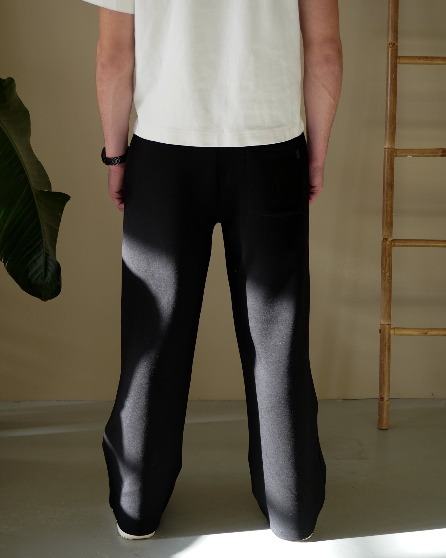 Person wearing black pants and a white shirt, standing with back to the camera, indoor setting.