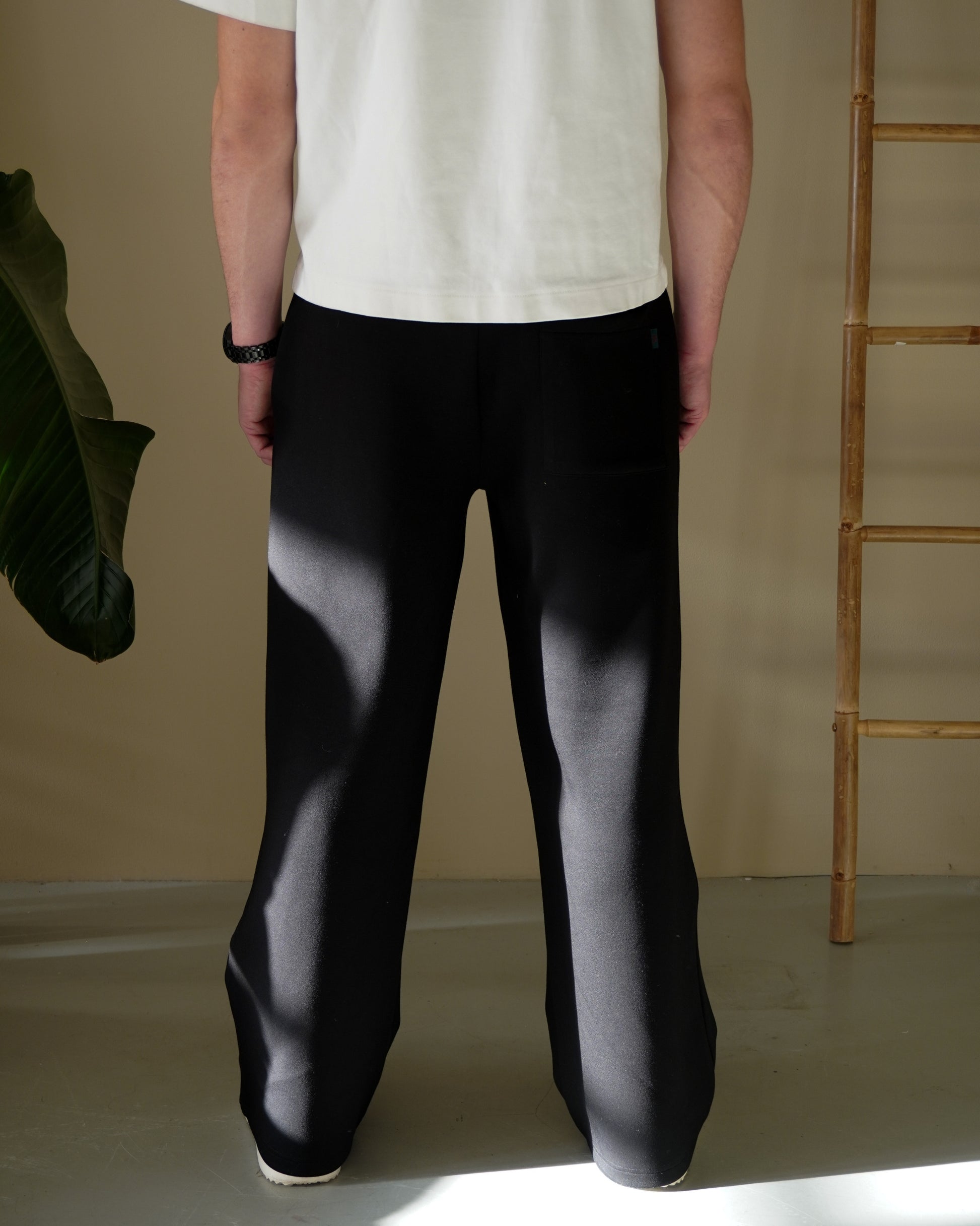 Person wearing black pants and a white shirt, standing with back to the camera, indoor setting.