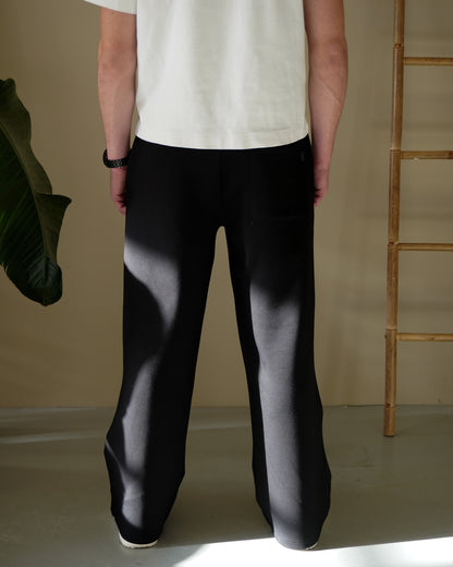 Person wearing black pants and a white shirt, standing with back to the camera, indoor setting.