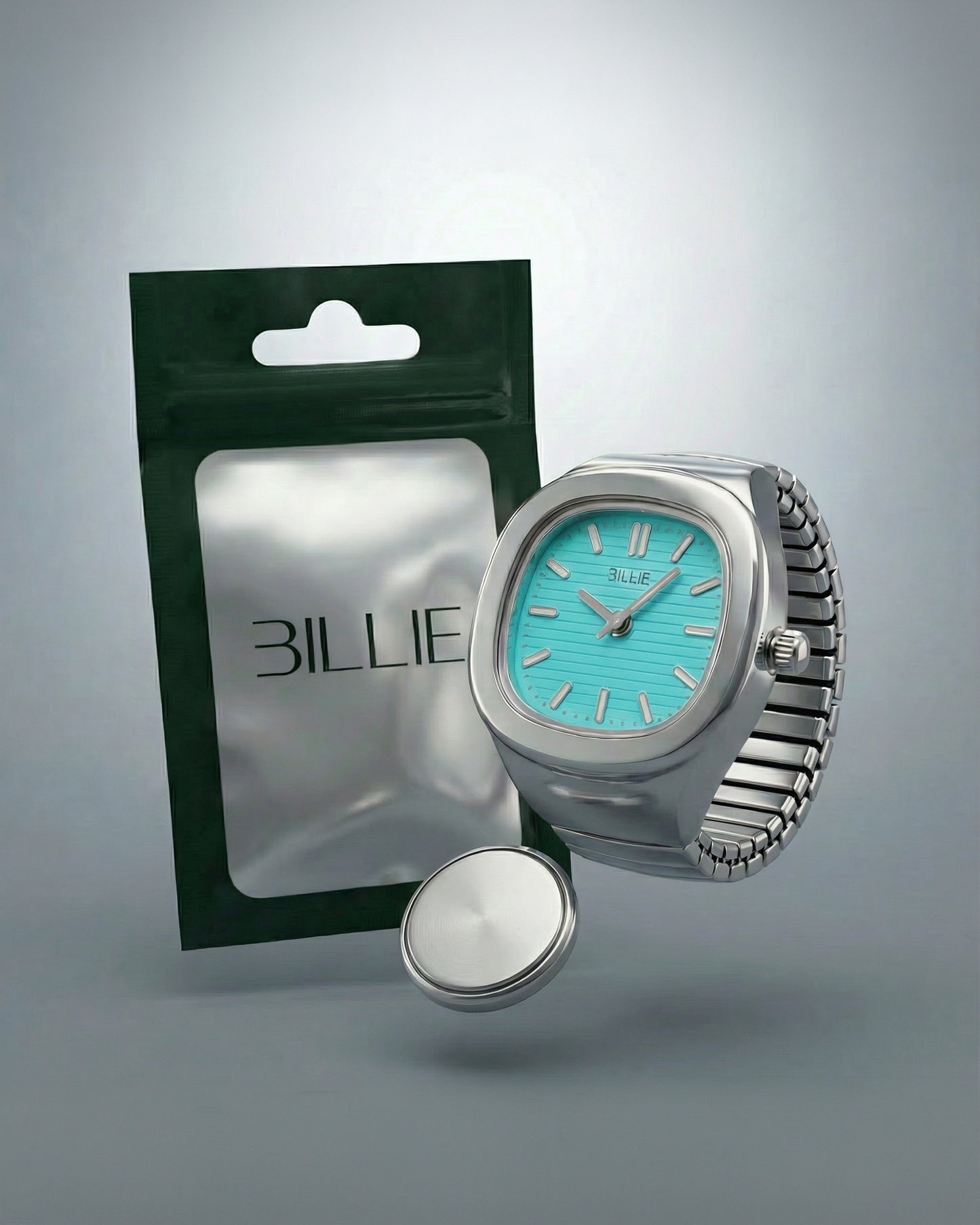 A silver watch with a turquoise face next to a green packaging and a round silver object.