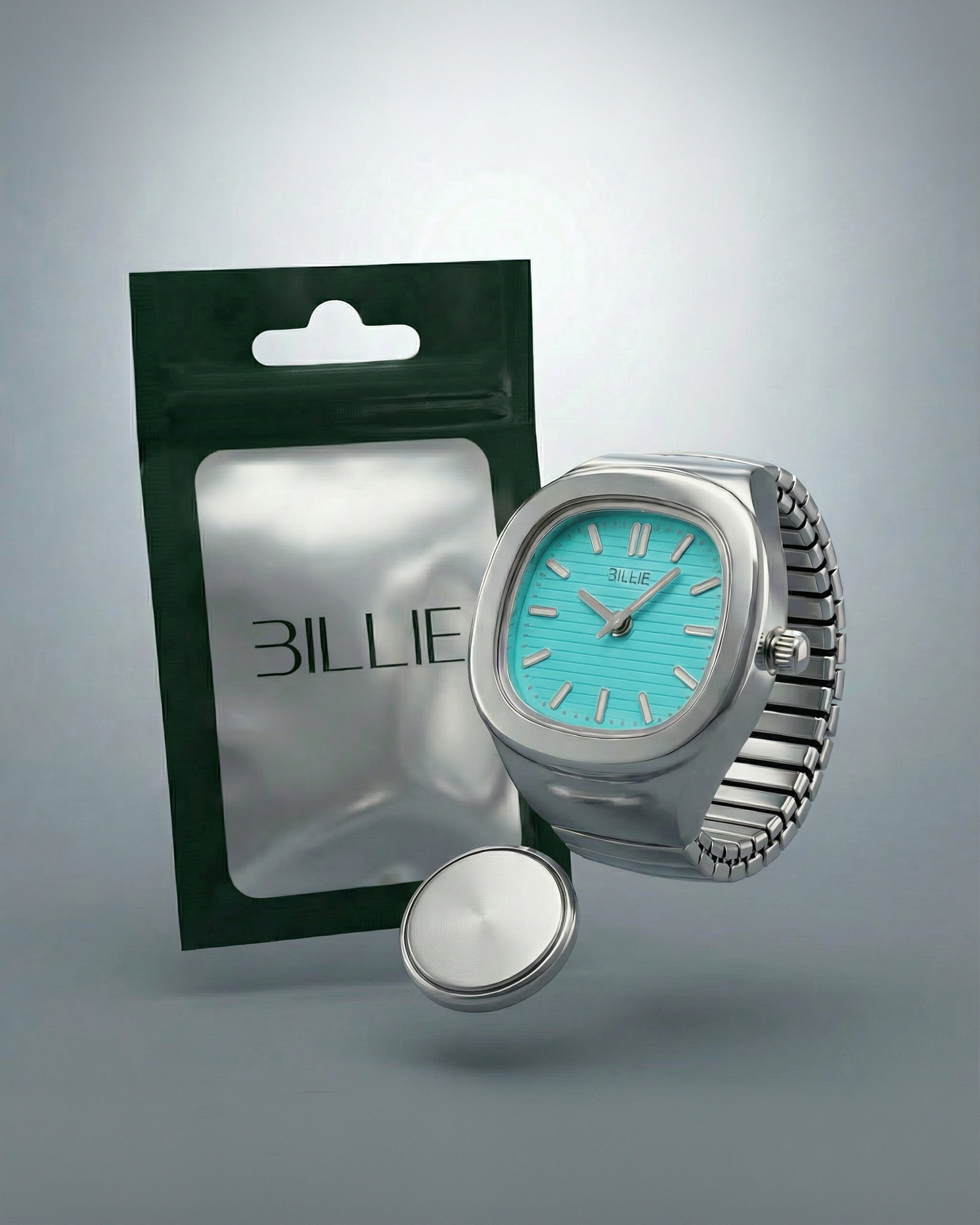A silver watch with a turquoise face next to a green packaging and a round silver object.