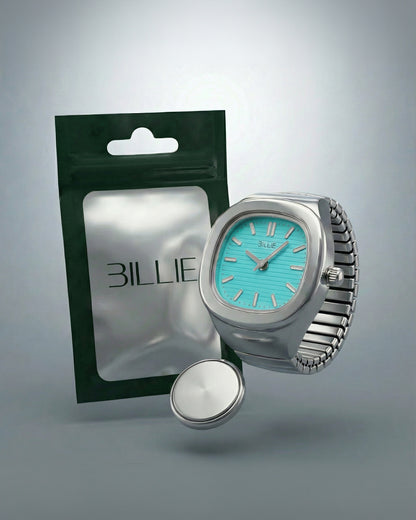A silver watch with a turquoise face next to a green packaging and a round silver object.