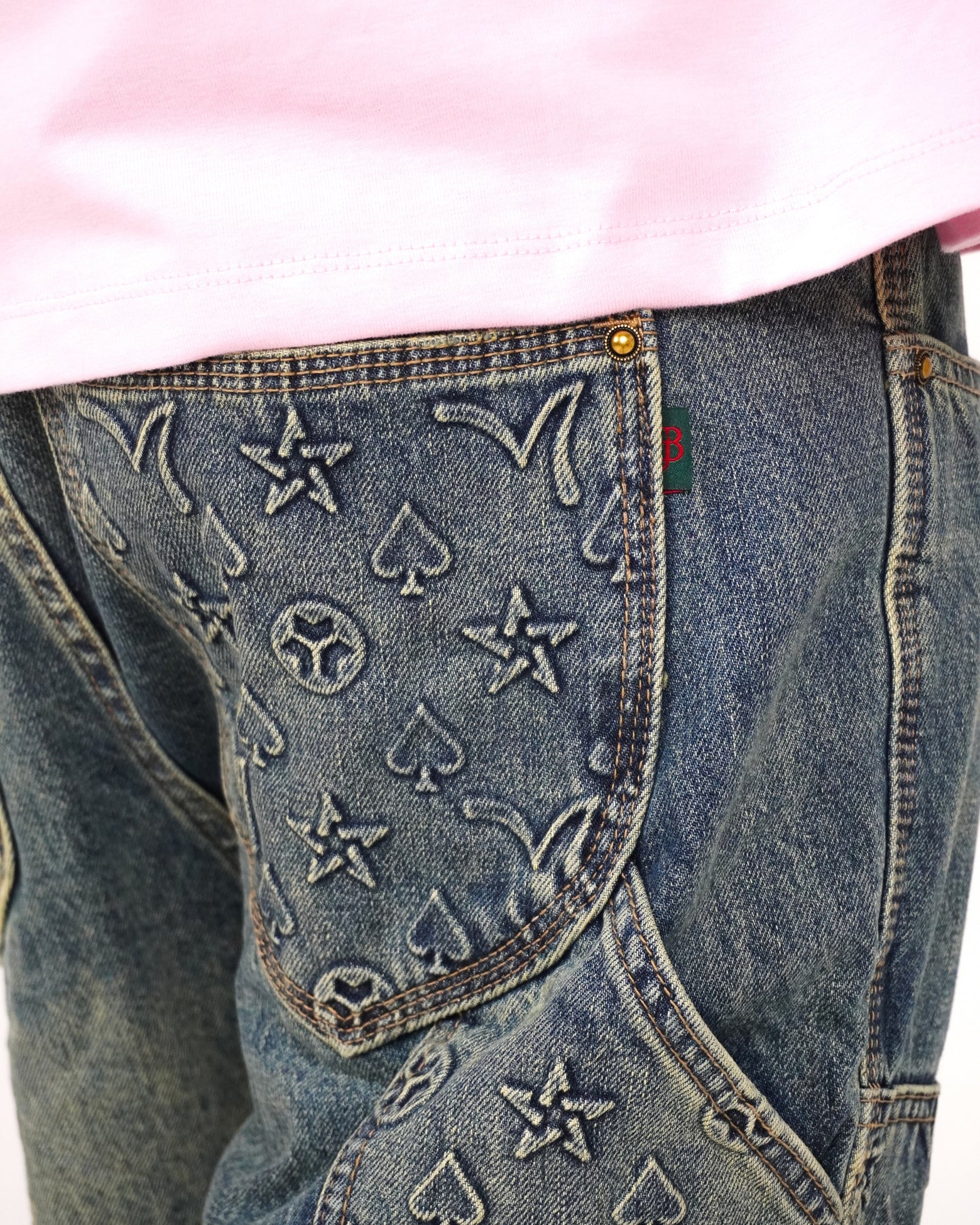 Close-up of denim with embossed star and spade patterns, partially covered by a pink shirt.