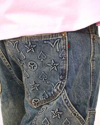 Close-up of denim with embossed star and spade patterns, partially covered by a pink shirt.