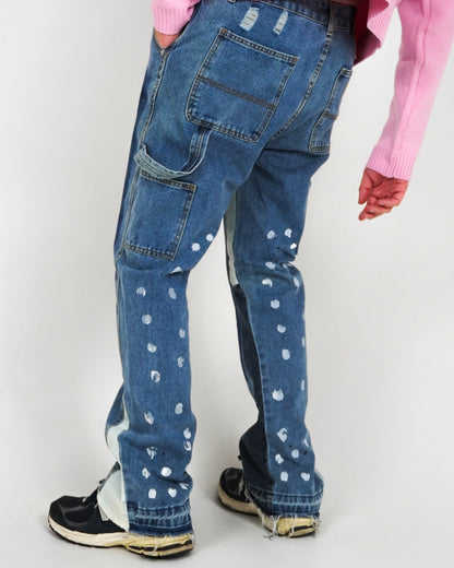 Person wearing blue jeans with paint splatters and a pink sweater, standing on a plain background.