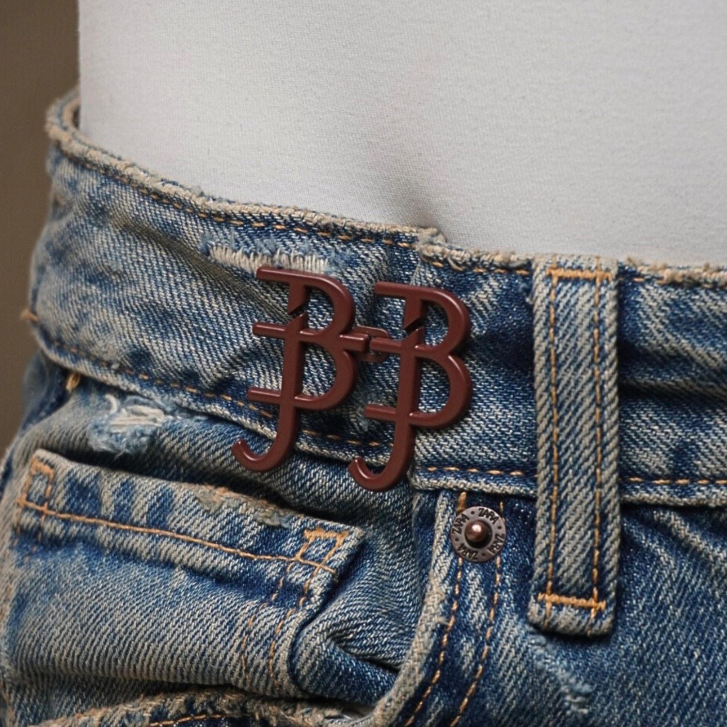 Close-up of blue jeans with a red belt buckle featuring a logo.