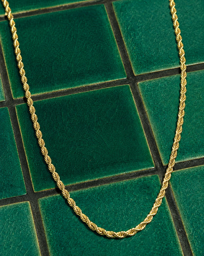 Gold twisted chain necklace on green tiled surface