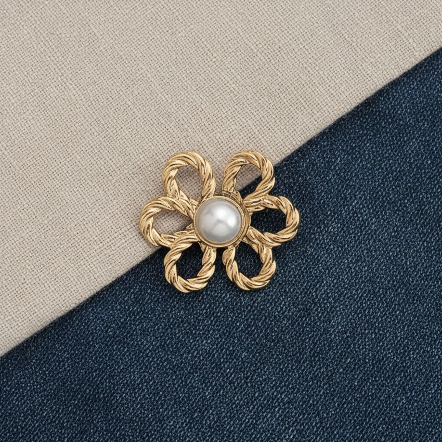 Gold flower-shaped brooch with a pearl center on a denim and beige fabric background