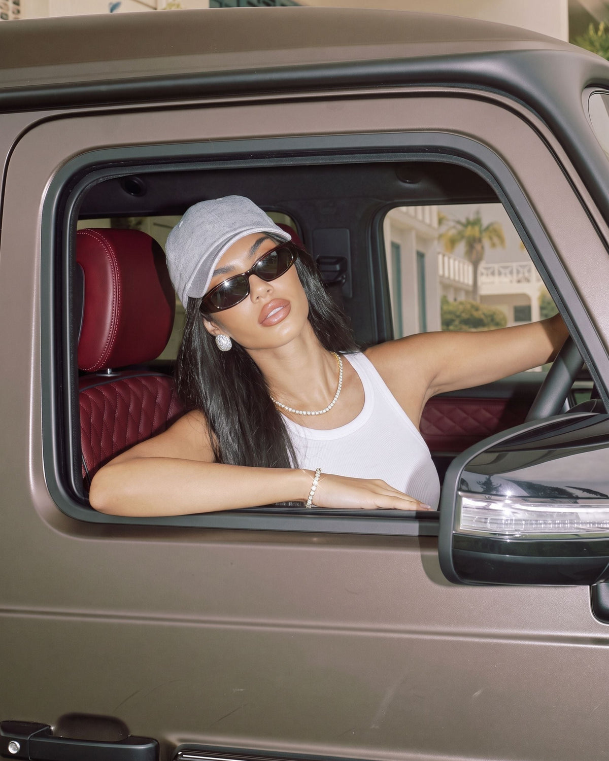 Woman in a grey cap and sunglasses wearing the gold Billie Tennis Bracelet 4mm leaning out of a car window