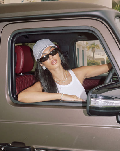 Woman in a grey cap and sunglasses wearing the gold Billie Tennis Bracelet 4mm leaning out of a car window