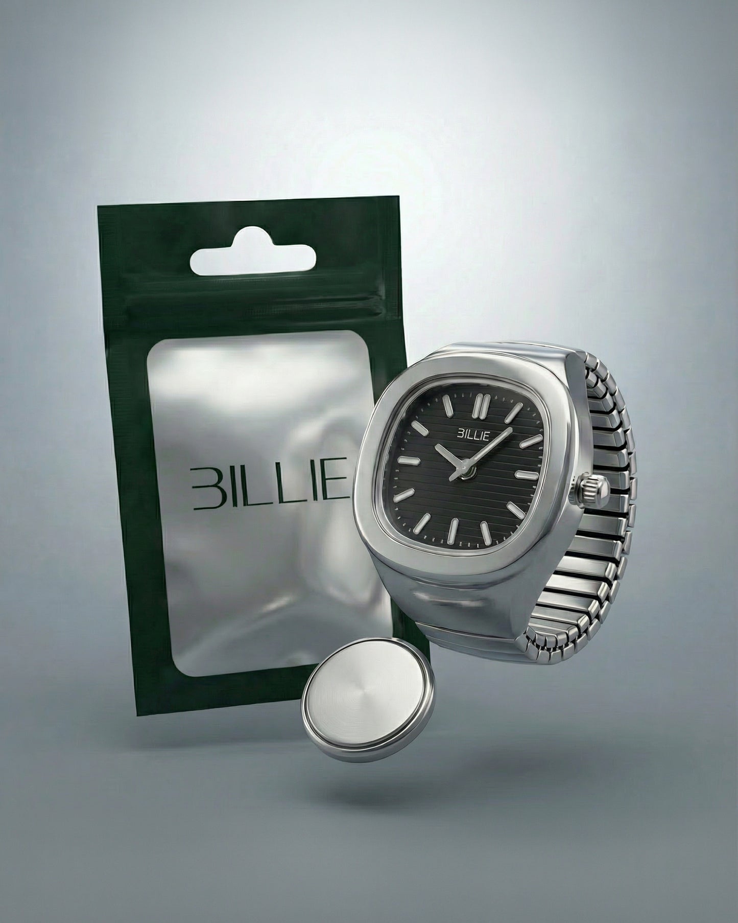 Silver watch with black dial next to a green packaging and a round silver object.