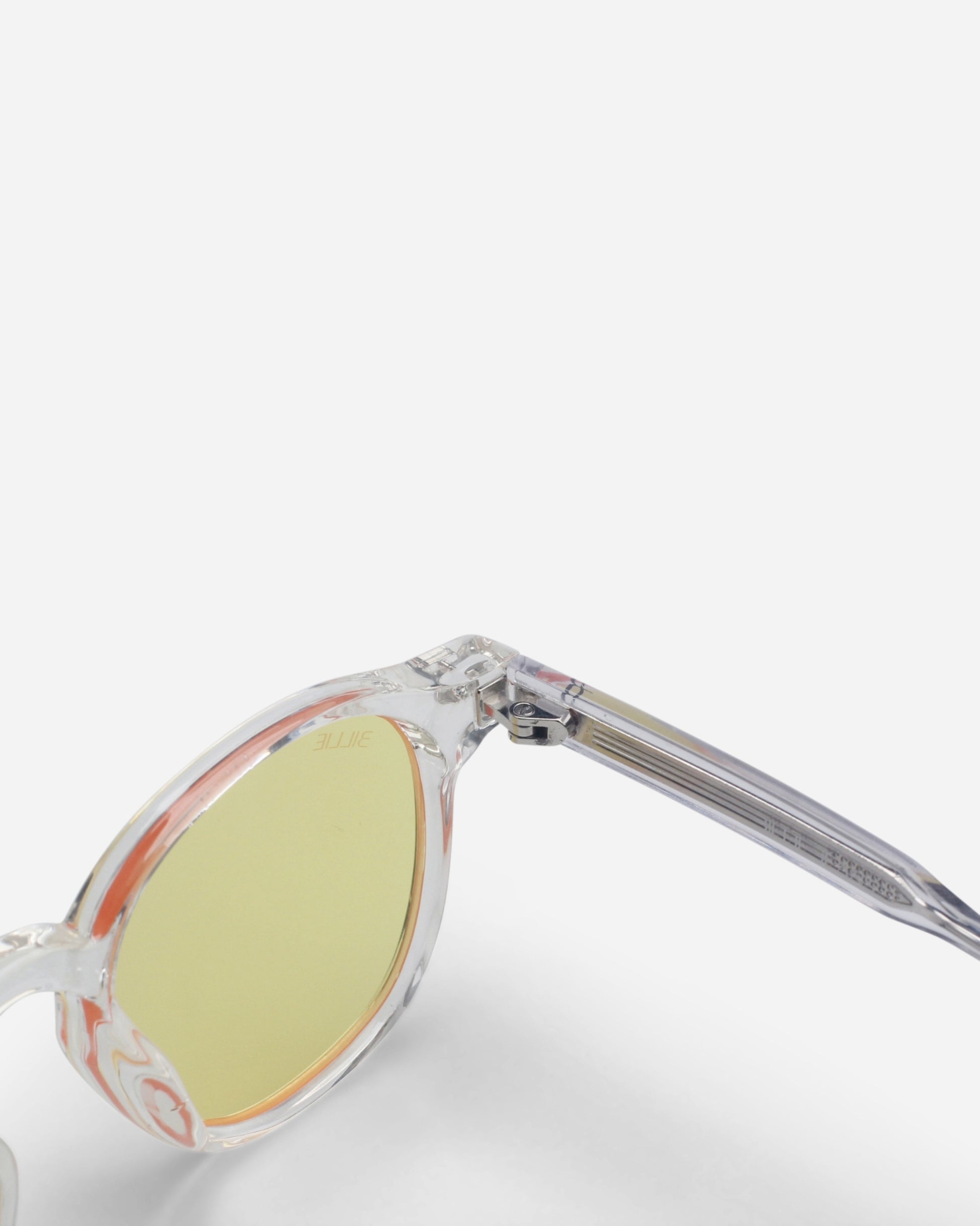Close-up of sunglasses with clear frames and yellow lenses on a plain background.