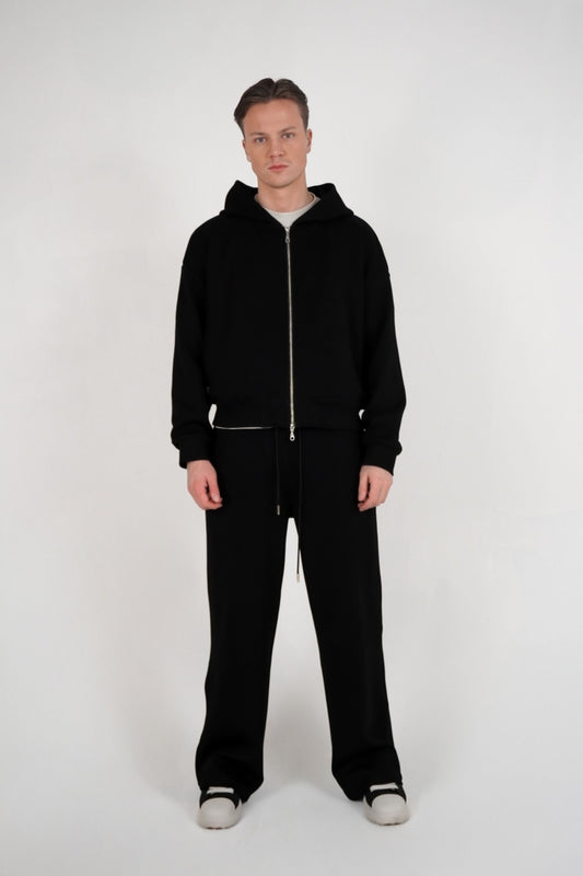 Person wearing a black hoodie and pants on a white background