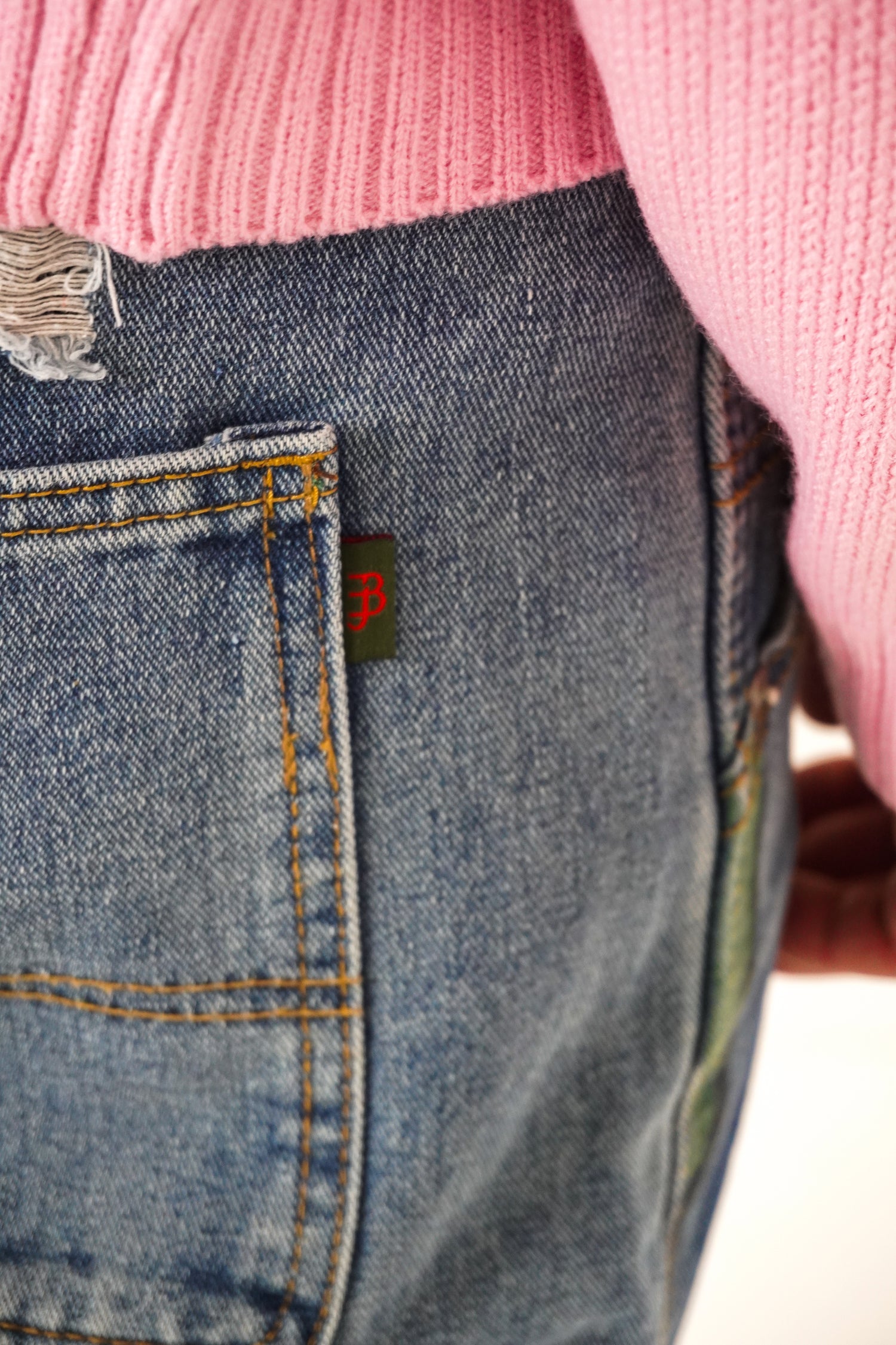Close-up of blue jeans with a brand logo on the pocket, worn with a pink sweater.