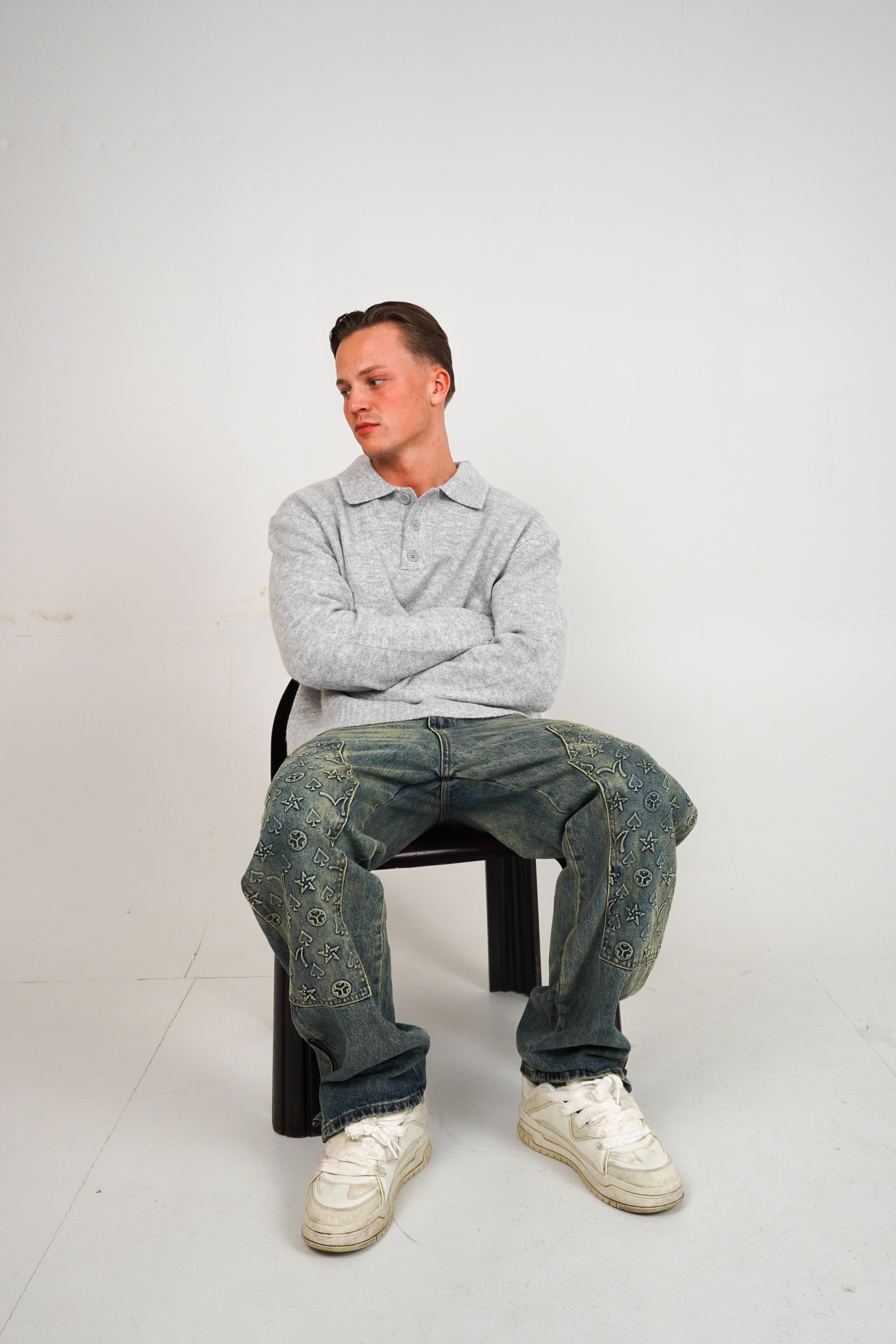 Person sitting on a chair wearing a gray sweater and blue jeans against a white background
