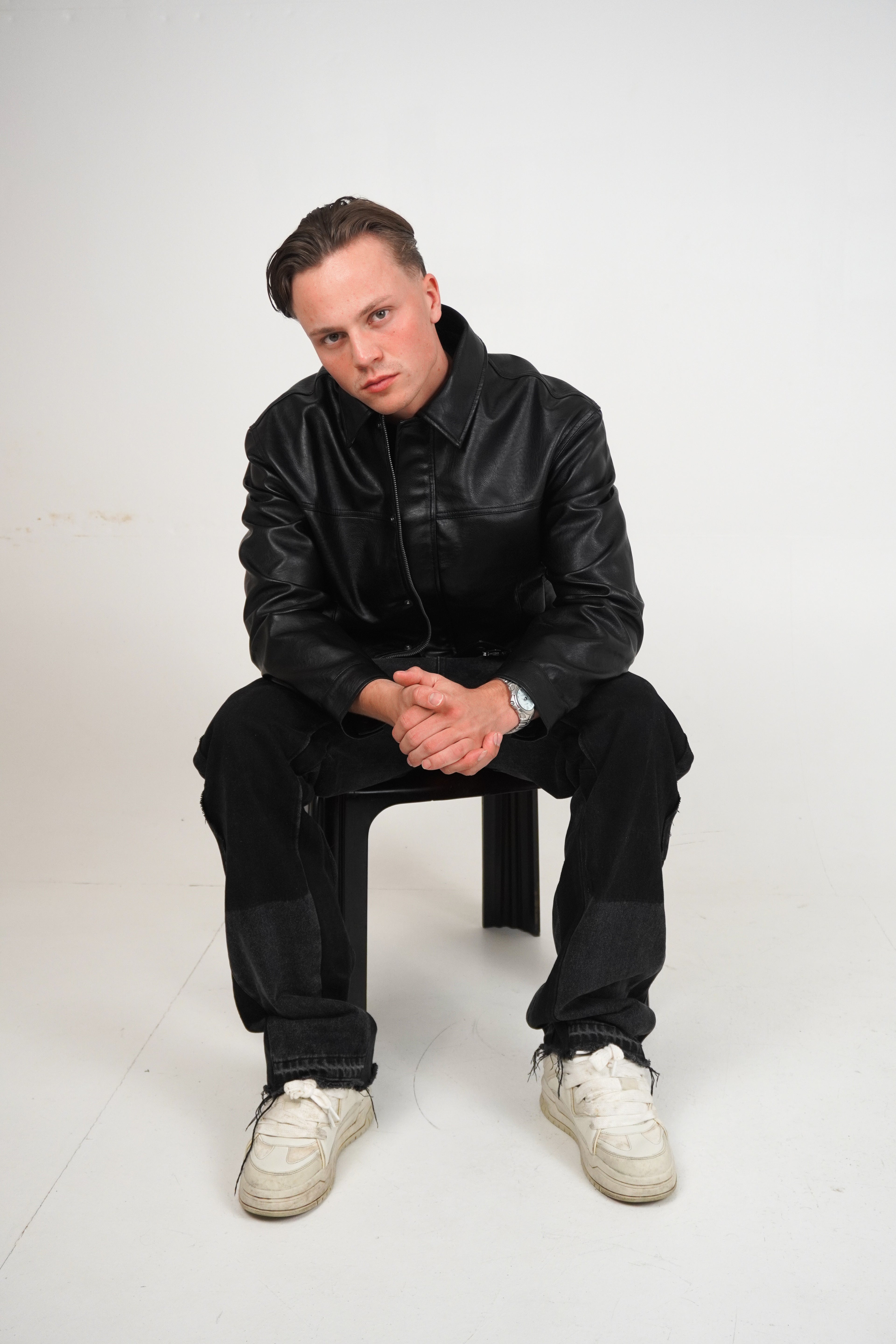 Person wearing a black outfit with white shoes sitting on a white background