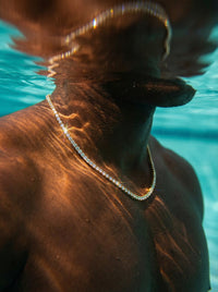 Person underwater wearing a gold chain necklace with clear water background