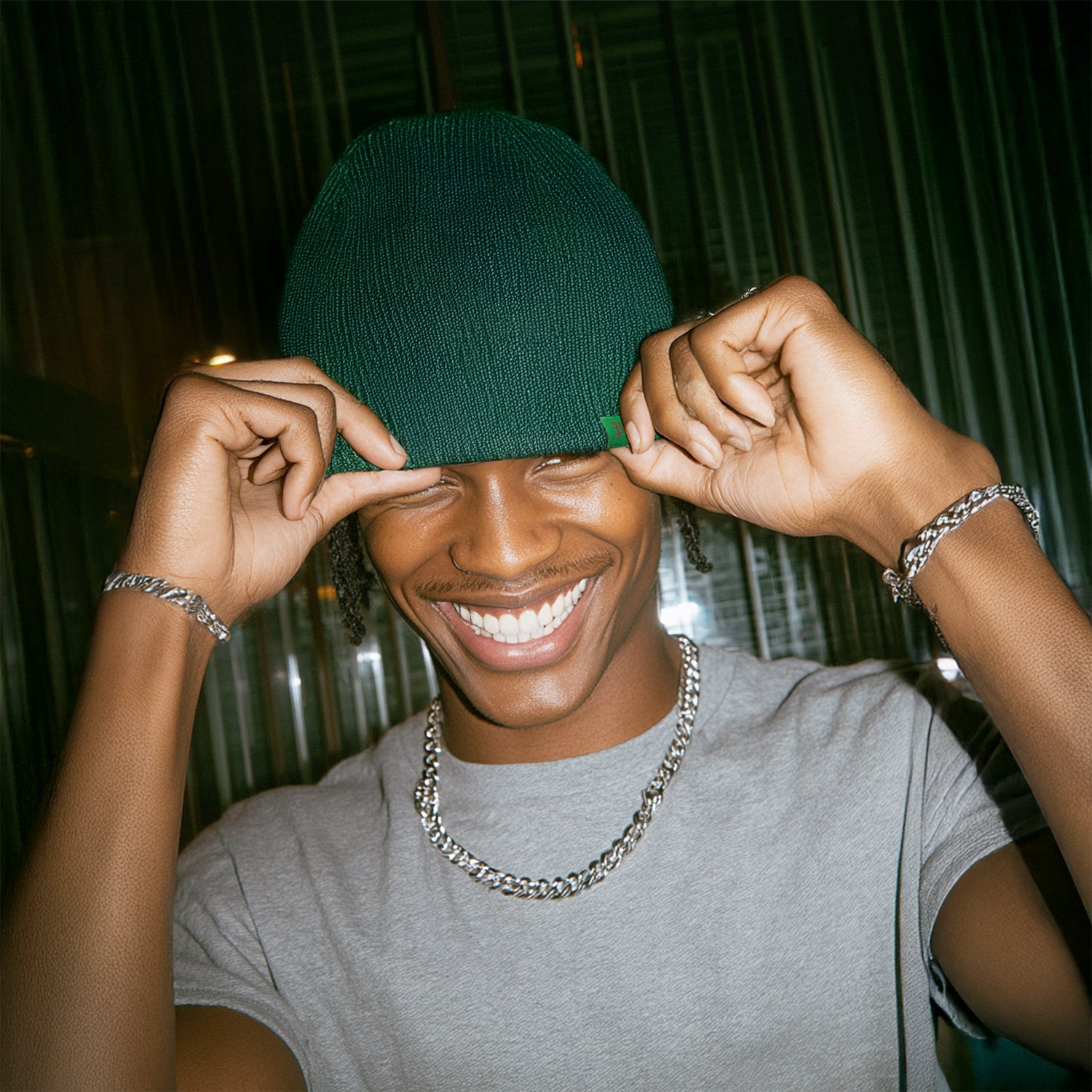 Person wearing a green beanie and gray shirt with a chain necklace, smiling.