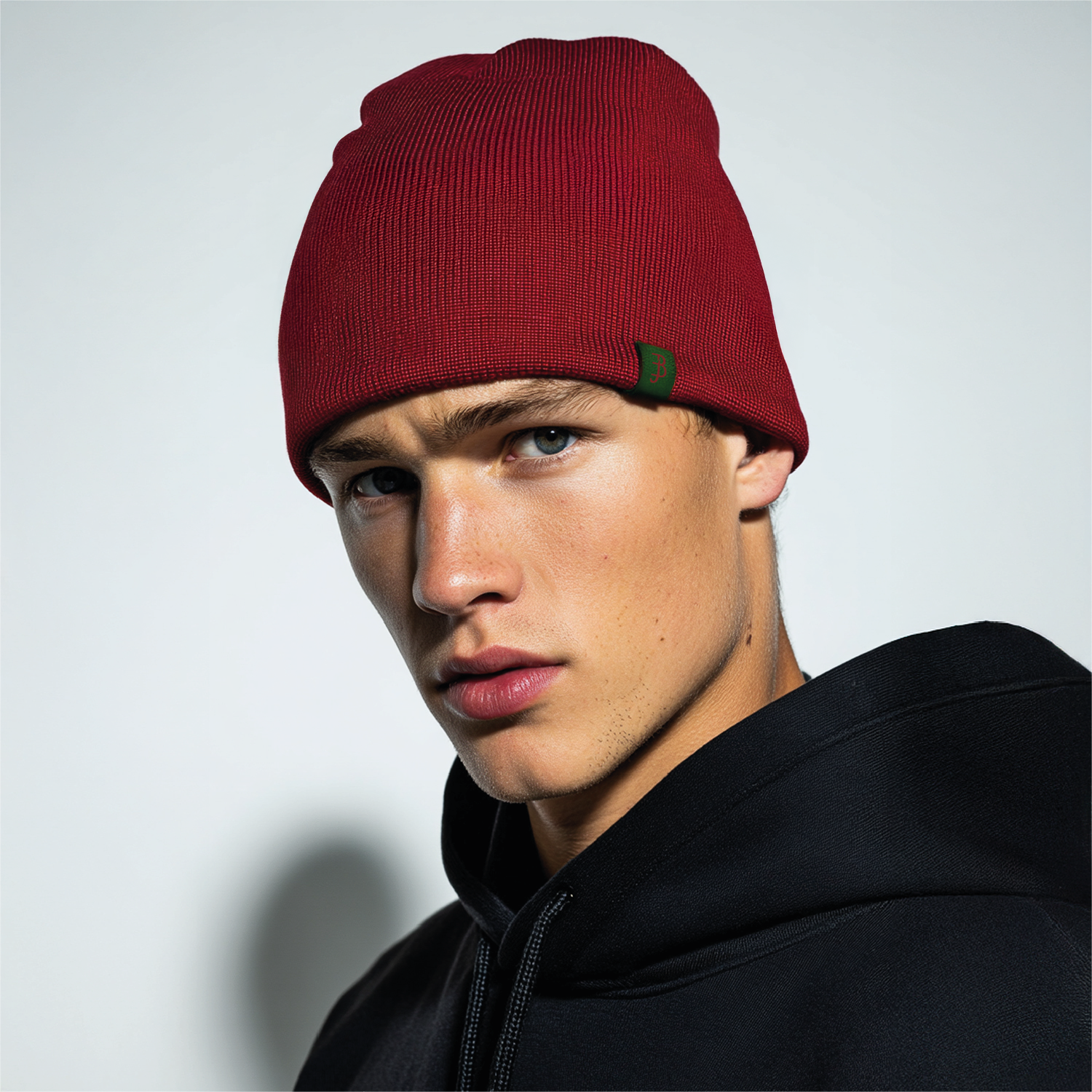 Man met een rode muts en een zwart jasje tegen een lichtgrijze achtergrond