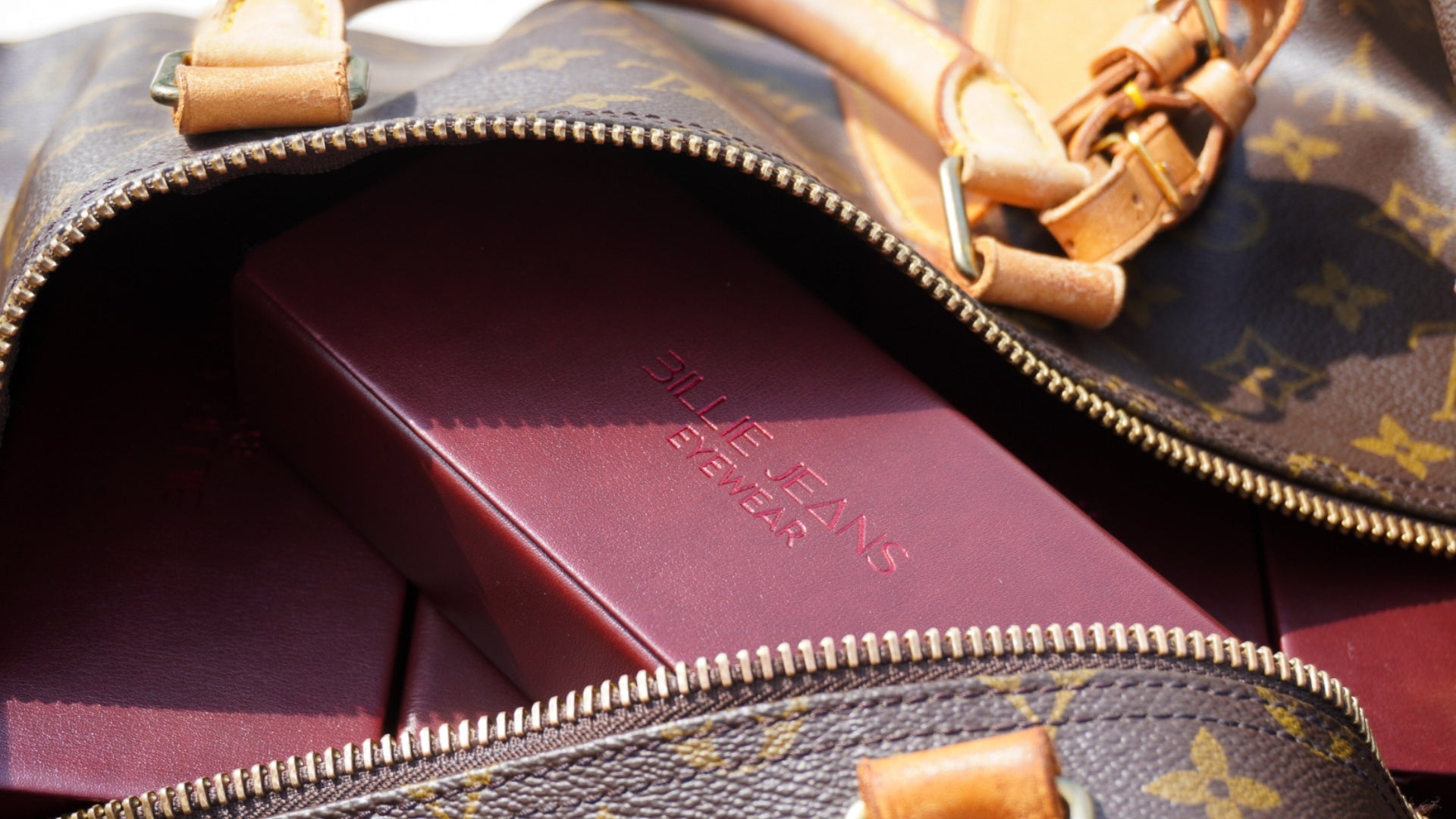 A close-up of an open Louis Vuitton monogram bag containing a burgundy presentation box embossed with the brand name 'LOUIS VUITTON'.