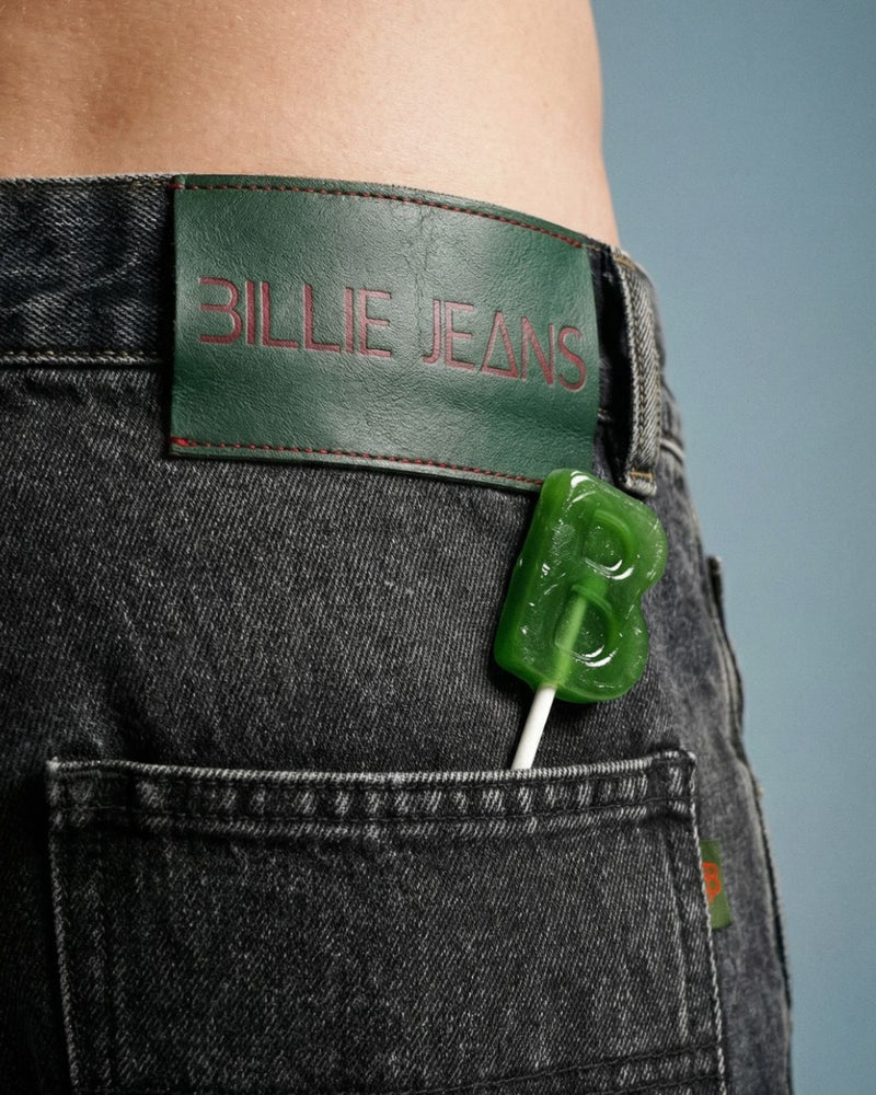 Green lollipop with 'B' logo in a pocket of black jeans with 'Billie Jeans' label.