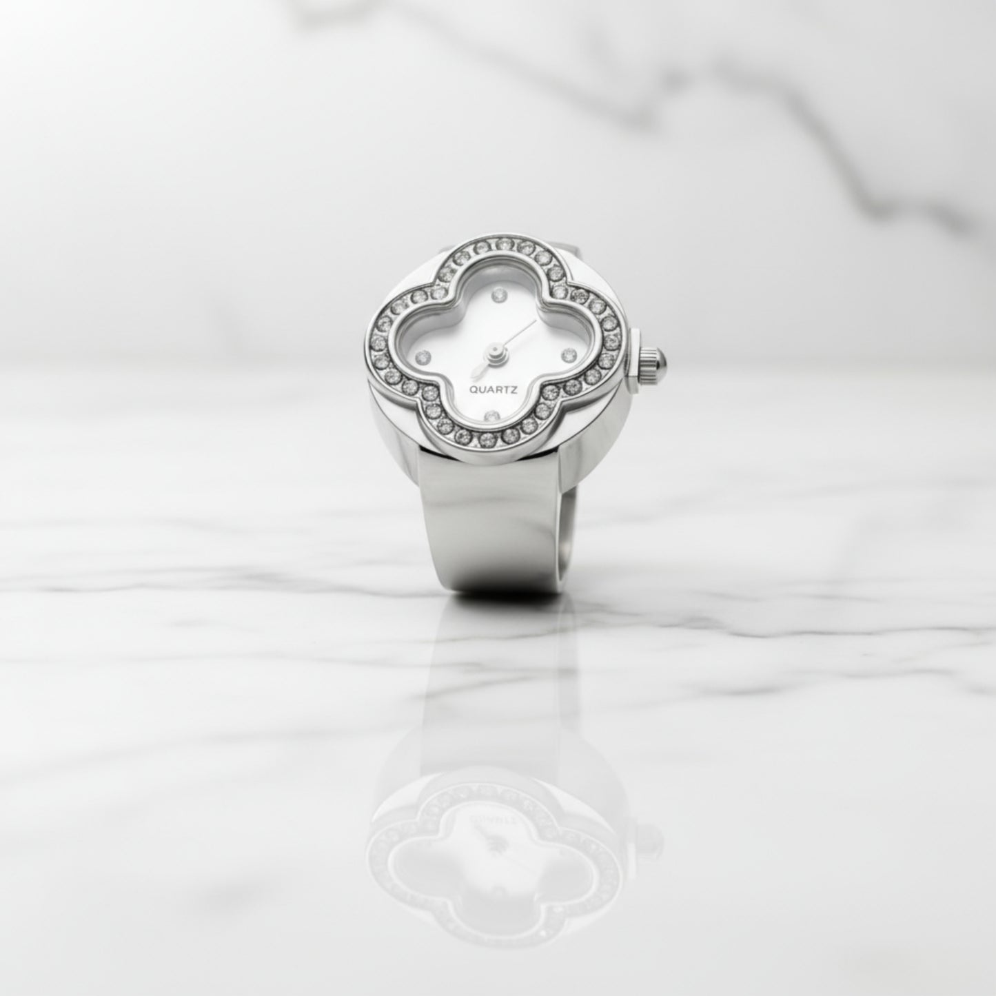 Silver ring watch with clover-shaped face on a white marble surface