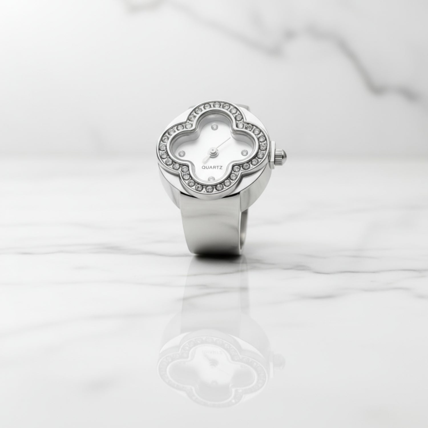 Silver ring watch with clover-shaped face on a white marble surface