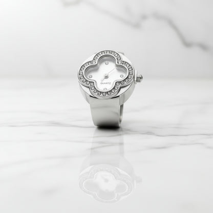 Silver ring watch with clover-shaped face on a white marble surface