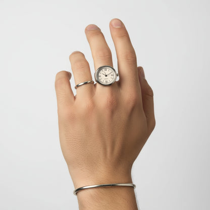 Hand wearing two silver rings with clock face designs on a light gray background