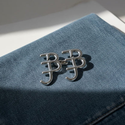 Silver brooch with 'B&J' initials on a blue fabric background